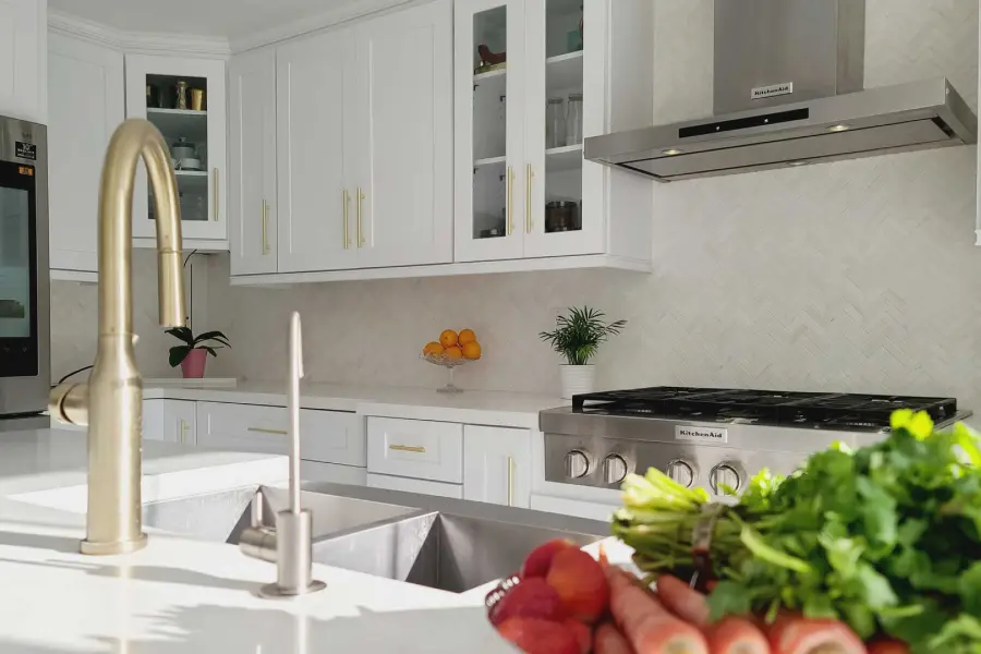 Close-up of a modern kitchen sink with a brushed gold faucet and a white herringbone backsplash.