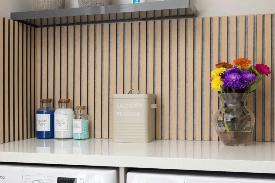 Contemporary laundry room with vertical wood panel backsplash, decorative storage jars, and a vase of vibrant flowers.