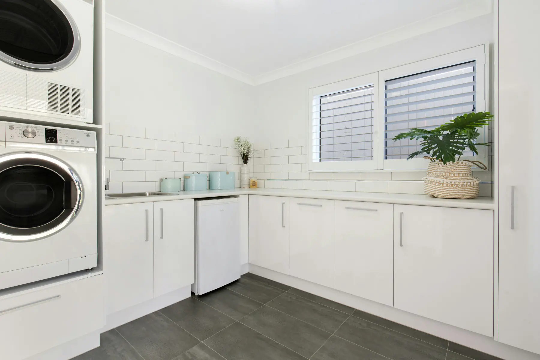 Bright laundry room featuring white tiled backsplash, stacked washer and dryer, and light decor accents.